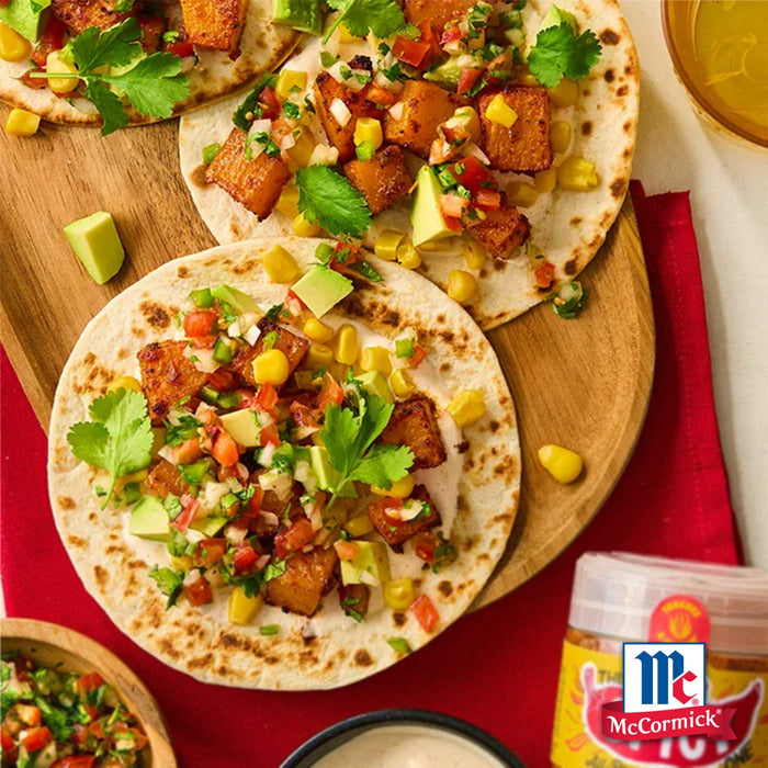 Eine Nahaufnahme zeigt McCormick's Taco-GewA?rz, das in einem lebendigen Gericht aus Tacos mit gewA?rztem Tofu, Mais, Avocado und Koriander verwendet wird, serviert auf einem Holzbrett.