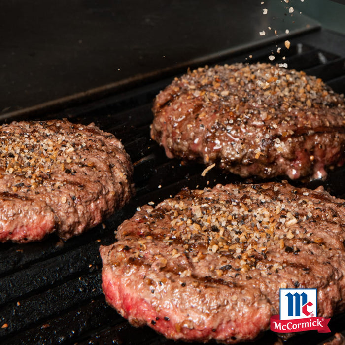 Drei gewürzte Hamburger-Patties, zubereitet mit Mccormick De Global Template All Rounders, grillen auf einem schwarzen Rost, mit dem McCormick-Logo sichtbar.