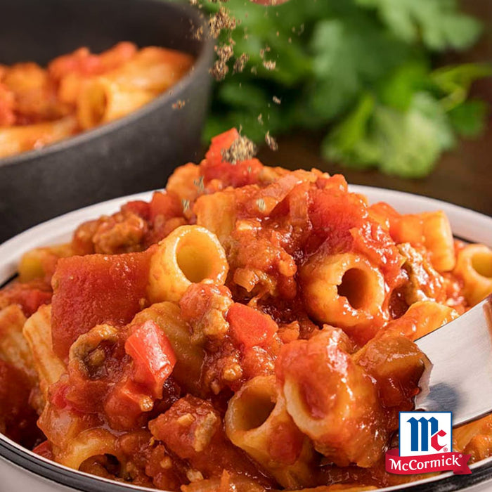 Eine Schüssel Rigatoni-Pasta mit einer reichhaltigen Tomatensauce und McCormick-Gewürzen, die darüber gestreut werden.