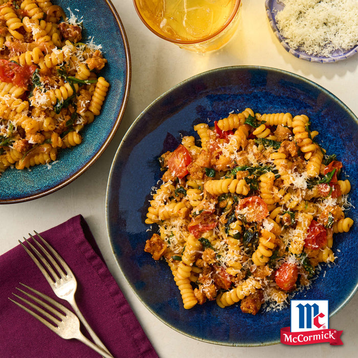 Zwei Teller Pasta mit GemA?se und McCormick-GewA?rzen werden auf einem Tisch mit Gabeln und einem Glas GetrA?nk prA?sentiert.