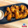 Das Bild von McCormick zeigt eine Platte mit glasierten Chicken Wings, serviert mit einem cremigen Dip.