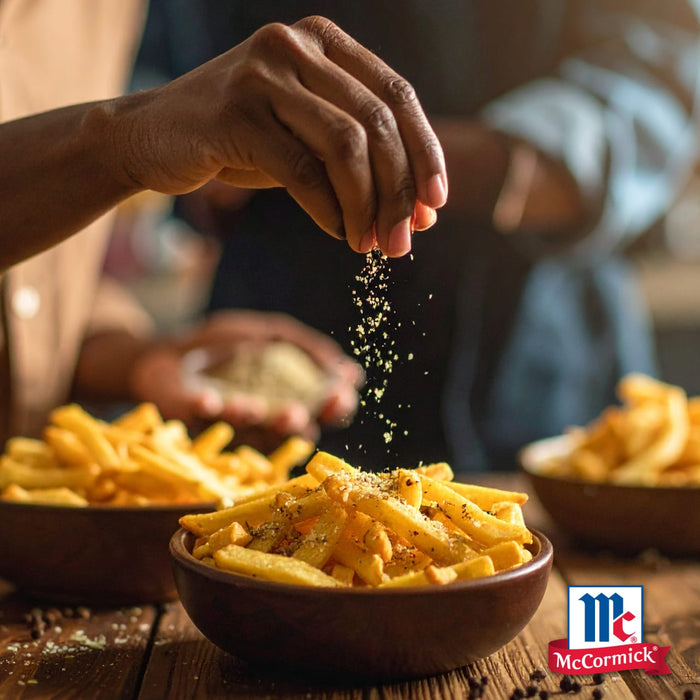 Eine Hand streut Gewürze auf eine Schüssel Pommes Frites, mit dem McCormick-Logo sichtbar, ein Bild, das zu Mccormick Global Template De gehört.