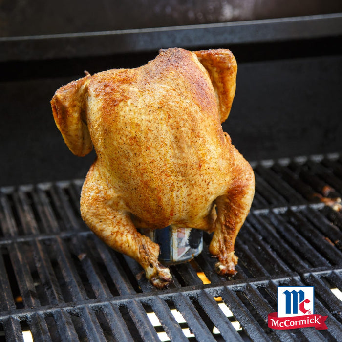 Ein ganzes Hähnchen das mit Srpet Chick Seas X06-Ge gewürzt wurde wird aufrecht auf einer Bierdose über einem heißen Grillrost mit dem McCormick Logo gegrillt.