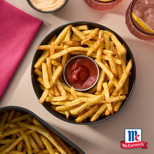 Eine Draufsicht auf eine Schüssel goldener Pommes Frites, die mit Srpet Chip Seas X06-Ge gewürzt und mit Ketchup serviert werden, mit dem McCormick-Logo.