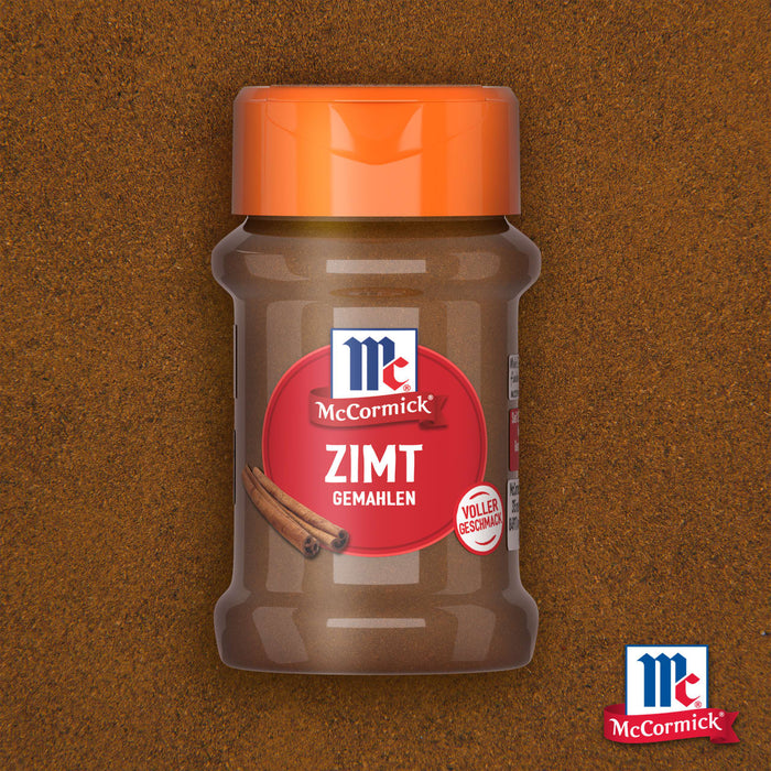 Ein Glas McCormick Srpet Cinnamon Gd X06-Ge gemahlener Zimt steht zentriert vor einem strukturierten Hintergrund aus demselben Gewürz.