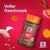 Eine Flasche Srpet Cinnamon Gd X06-Ge von McCormick wird vor einem leuchtend roten Hintergrund präsentiert umgeben von schwebenden Zutaten wie Zimtstangen und Knoblauch