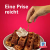 Eine Hand streut eine Prise Srpet Cinnamon Gd X06-Ge über einen Teller mit goldbraunen Waffeln und Schlagsahne vor einem roten Hintergrund mit dem McCormick Logo.