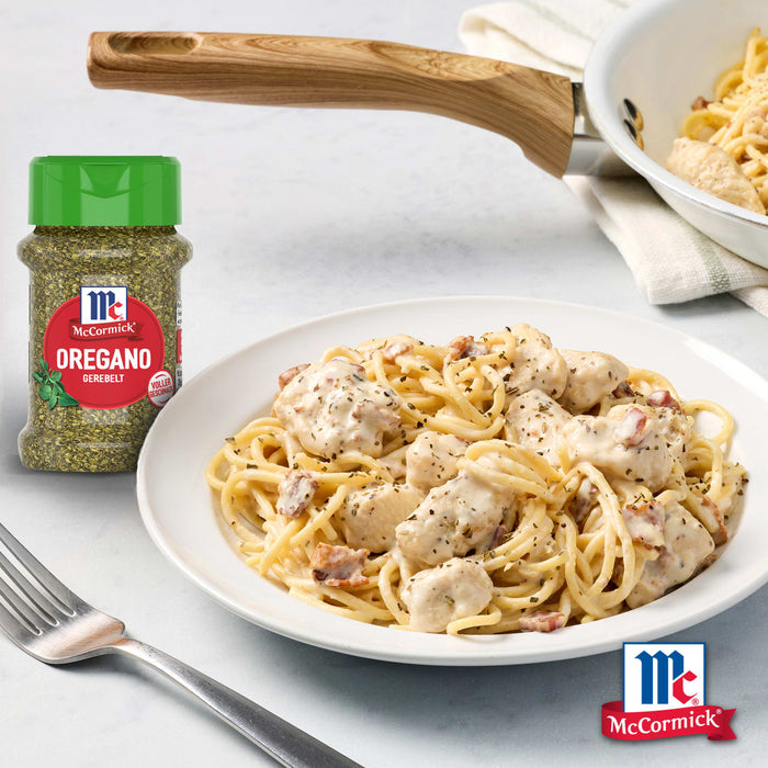 Ein Teller cremiger Hähnchen-Speck-Pasta wird mit Srpet Oregano X06-Ge aus einer daneben stehenden McCormick-Flasche verfeinert.