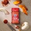 Eine Flasche Srpet Paprika Sweet X06-Ge ist von frischen Zutaten wie Knoblauchzehen und geschnittenen Kurkumawurzeln umgeben um das reiche Geschmacksprofil hervorzuheben.