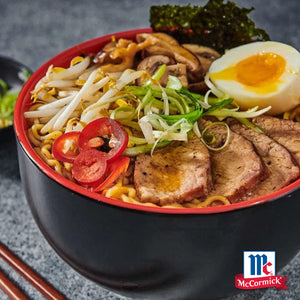Eine dampfende Schüssel Ramen, belegt mit Schweinefleischscheiben, einem weichgekochten Ei und frischem Gemüse, ist mit Srpet Bl Pepper Gd X06-Ge gewürzt und zeigt das McCormick-Logo.