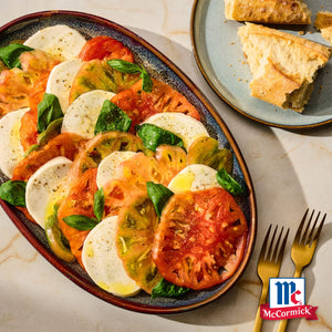 Eine lebendige Platte mit Srpet Tomato Mozza X06-Ge mit abwechselnden Scheiben von Heirloom Tomaten und frischem Mozzarella Käse garniert mit Basilikumblättern und einem McCormick Logo.