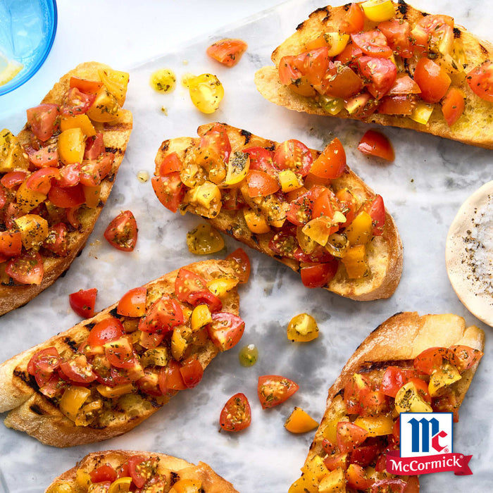 Eine Marmoroberfläche beherbergt mehrere Stücke geröstetes Brot, die mit einer farbenfrohen Mischung aus roten und gelben Tomaten belegt sind, die mit Srpet Tomato Mozza X06-Ge und dem McCormick-Logo in der Ecke gewürzt sind.