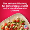 Eine lebendige Anzeige für Srpet Tomato Mozza X06-Ge von McCormick zeigt Spieße mit frischen Kirschtomaten und Mozzarellakugeln, die mit Kräutern und Olivenöl auf einem kräftigen roten Hintergrund angerichtet sind.