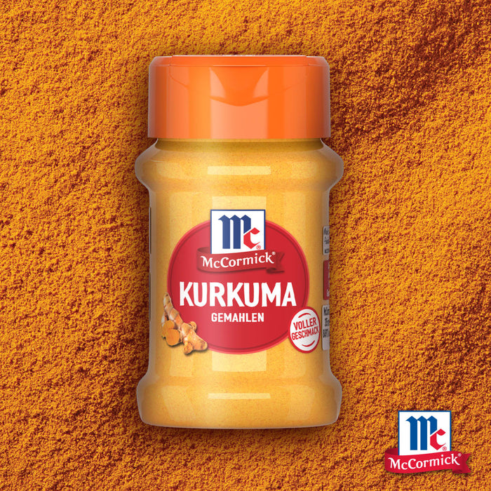 Eine Flasche McCormick Srpet Turmeric X06-Ge gemahlener Kurkuma steht zentriert vor einem strukturierten Hintergrund aus leuchtend orangefarbenem Gewürzpulver.