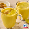 Zwei Glastassen gefüllt mit einem warmen Golden Milk Latte aus Srpet Turmeric X06-Ge sind mit einer Prise Gewürz garniert und neben einem Honiglöffel und dem McCormick Logo abgebildet.